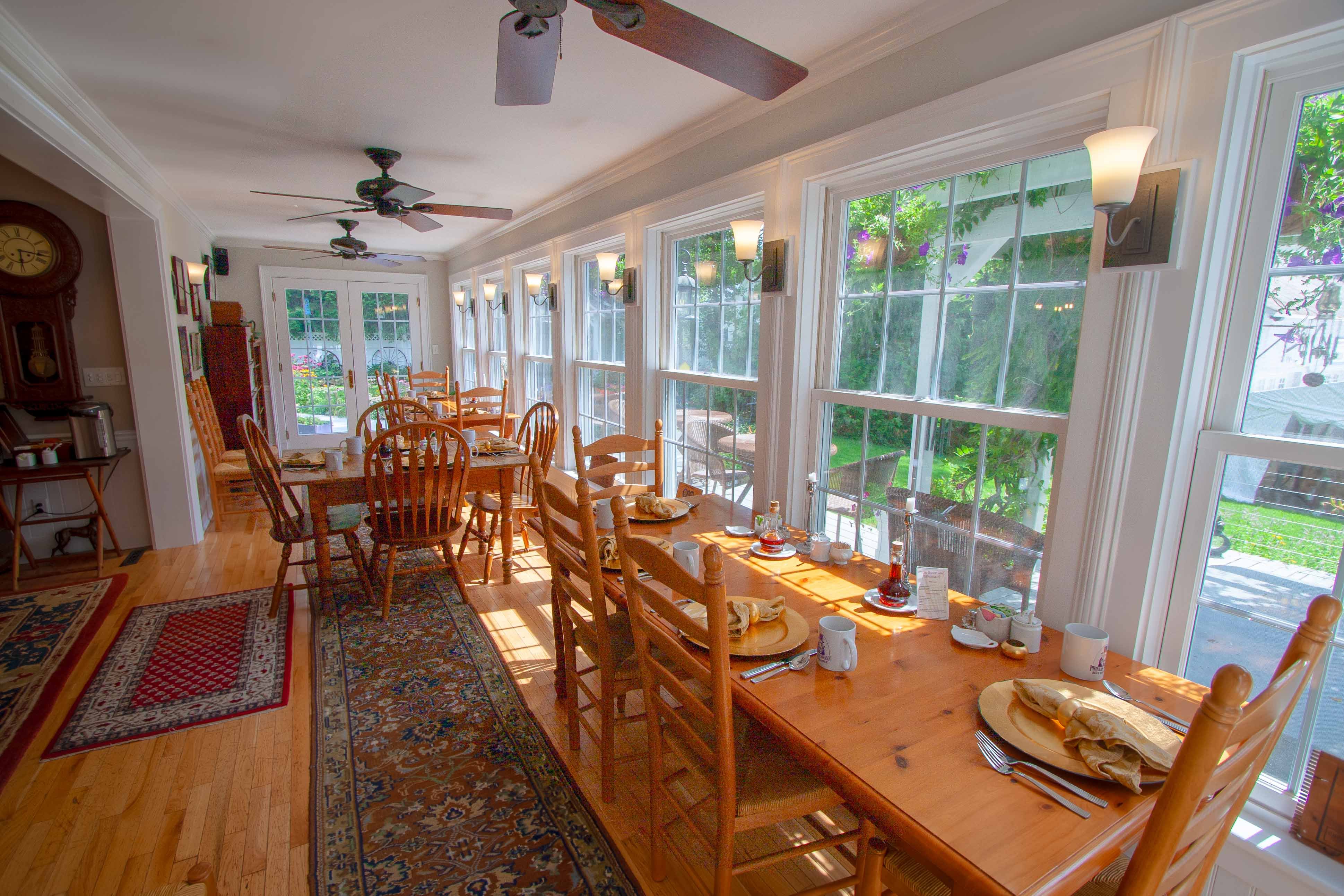 Bright dining room with wooden tables, chairs, and large windows overlooking a garden.