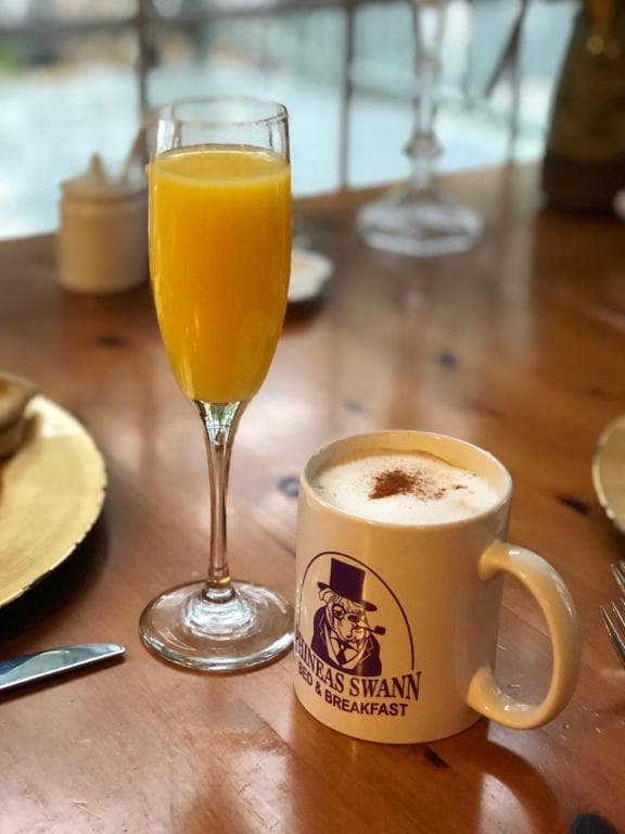 A glass of mimosa next to a coffee cup with a logo on a wooden table.