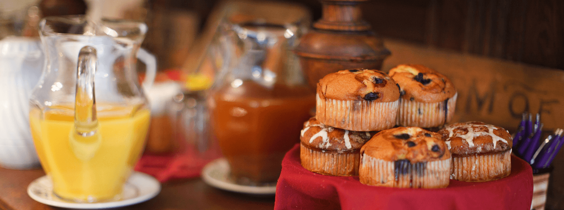 A display of muffins on a red cloth with pitchers of orange juice and another beverage in the background.
