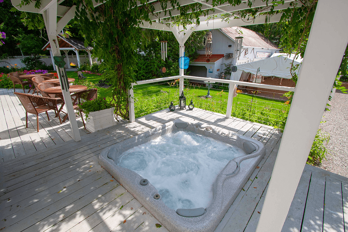 A hot tub bubbling under a covered gazebo surrounded by a lush garden.