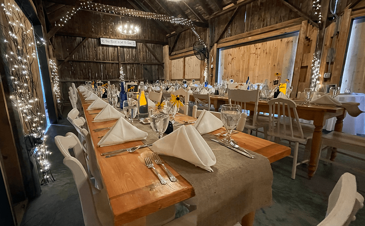 A beautifully set dining table in a rustic barn, adorned with simple decor and warm lighting.