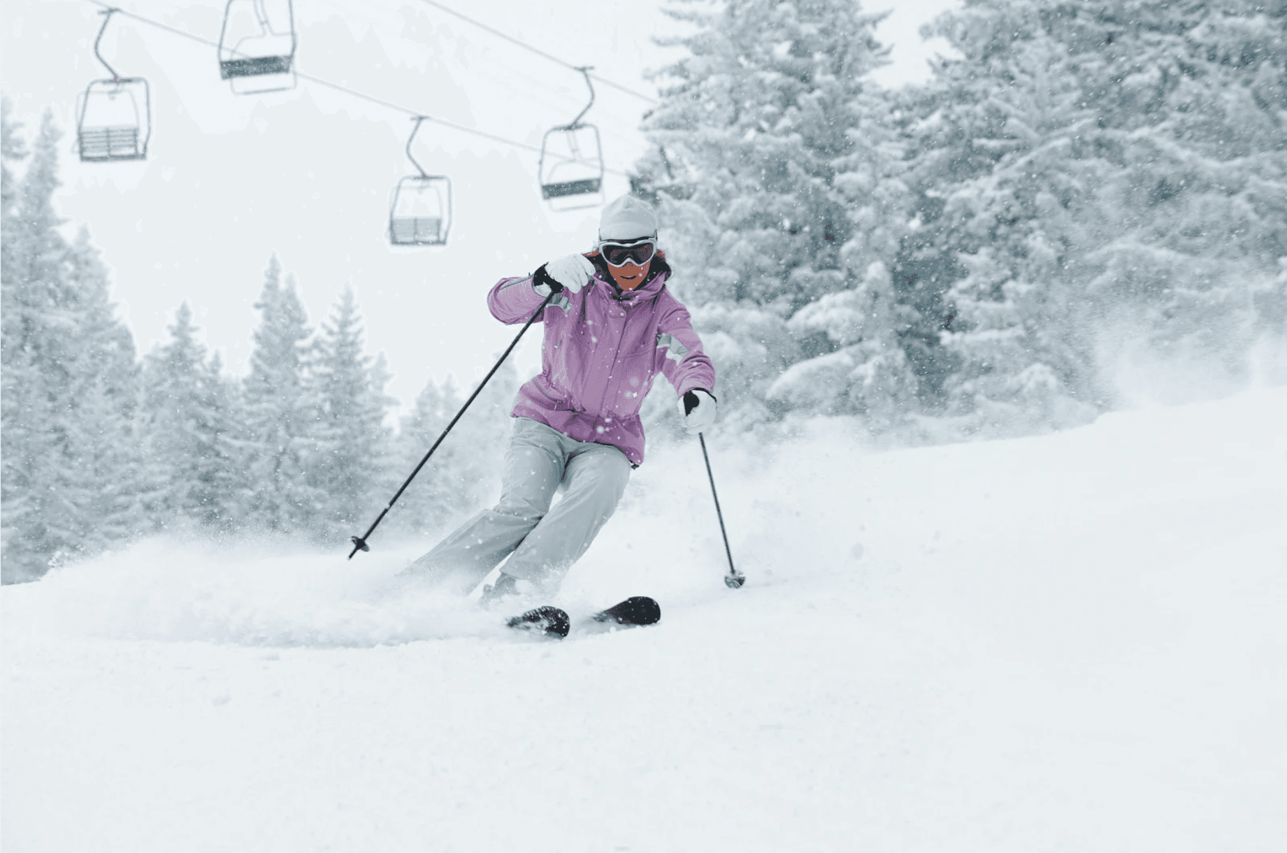 A skier in a pink jacket gracefully turns on a snowy slope with chairlifts in the background.